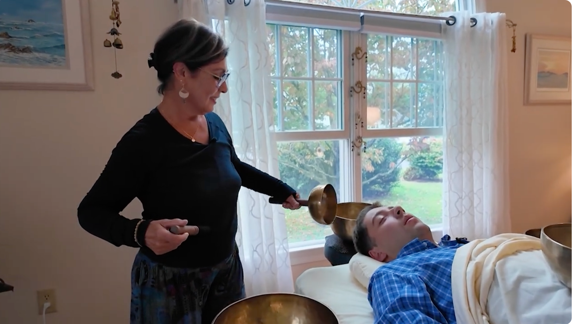 Woman performing sound healing therapy with singing bowls on a relaxed person indoors.